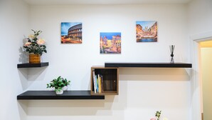 A room with three paintings depicting famous landmarks, a bookshelf with books, and two potted plants on shelves. - Vatican Area Apartment with 2 Bedrooms and 2 Baths (Roma)