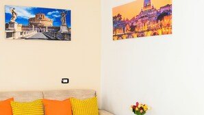 A room with a white table, orange cushions, a vase with flowers, and two cityscape paintings on the wall. - Vatican Area Apartment with 2 Bedrooms and 2 Baths (Roma)