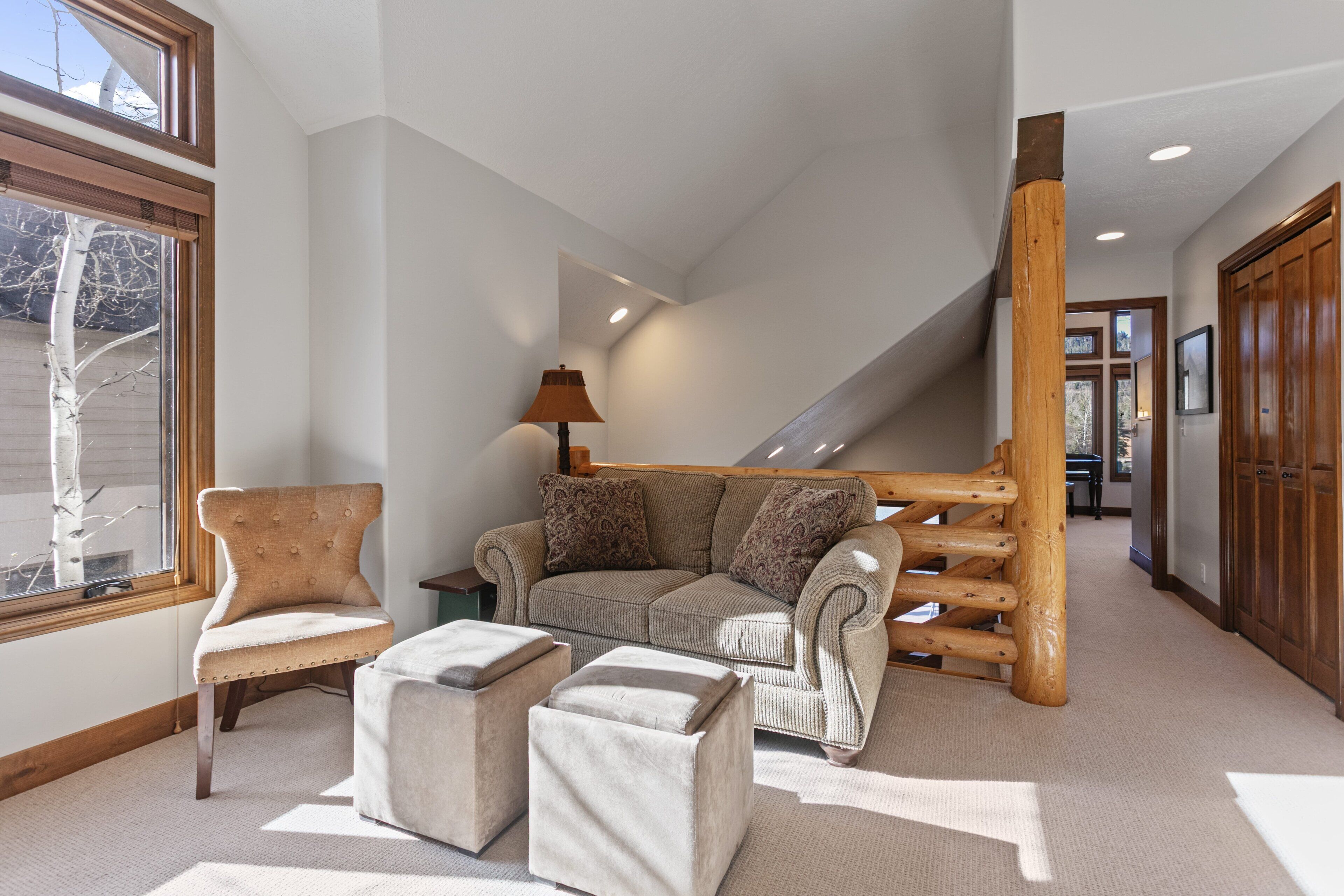 Ein modernes Interieur mit Sofa, Hocker und Sessel in der Nähe eines Fensters, einer Treppe und Holzakzenten.