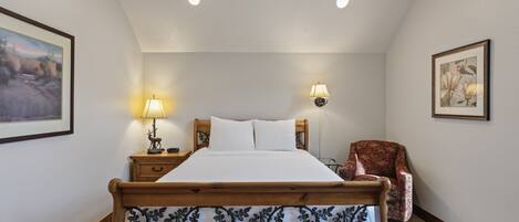A bedroom with a wooden bed, two bedside lamps, a chair, and framed artwork on the walls.