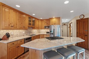 A kitchen with wooden cabinets, a granite countertop, stainless steel appliances, and a bar area with stools. - Deer Valley Townhome Walkable Location + Hot Tub 3 Bedroom Condo (Park City)