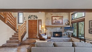 Una sala de estar con chimenea, una pared de piedra, una escalera de madera y un ventanal grande.