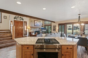 A kitchen with a large island, wooden cabinets, a gas stove, and a stone fireplace. - Deer Valley Townhome Walkable Location + Hot Tub 3 Bedroom Condo (Park City)