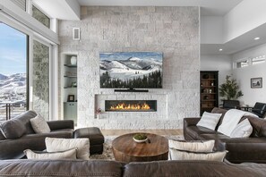 A modern living room with a stone fireplace, leather sofas, a round coffee table, and a large flat-screen TV mounted on the wall. - Luxury Deer Valley East Village Home + Hot Tub 6br 6 Bedroom Home (Heber City)