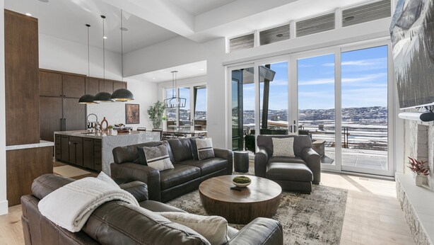 A spacious living area with a large sofa, a coffee table, and a view of the city through large windows. - Luxury Deer Valley East Village Home + Hot Tub 6br 6 Bedroom Home (Heber City)