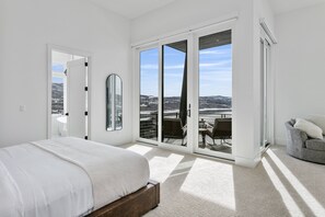 Een slaapkamer met een bed, een grote spiegel en een schuifdeur naar een balkon met zitplaatsen.
