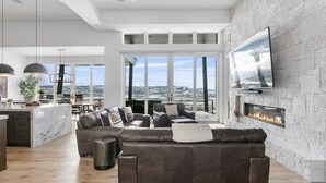 A modern living room with a fireplace, leather sofa, and a large TV on the wall. - Luxury Deer Valley East Village Home + Hot Tub 6br 6 Bedroom Home (Heber City)