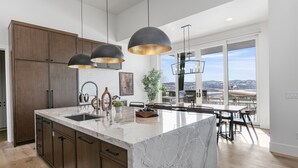 A modern kitchen with a large island, pendant lighting, and a view of the city. - Luxury Deer Valley East Village Home + Hot Tub 6br 6 Bedroom Home (Heber City)
