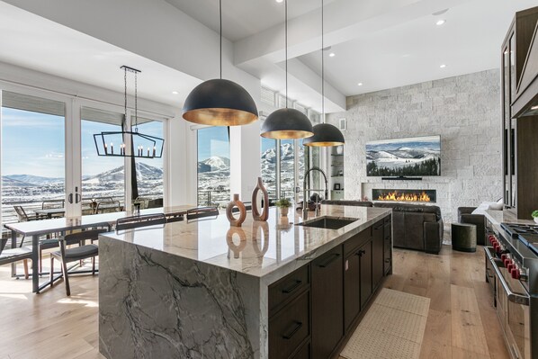 A modern kitchen with a large island, pendant lights, a fireplace, and a view of mountains. - Luxury Deer Valley East Village Home + Hot Tub 6br 6 Bedroom Home (Heber City)