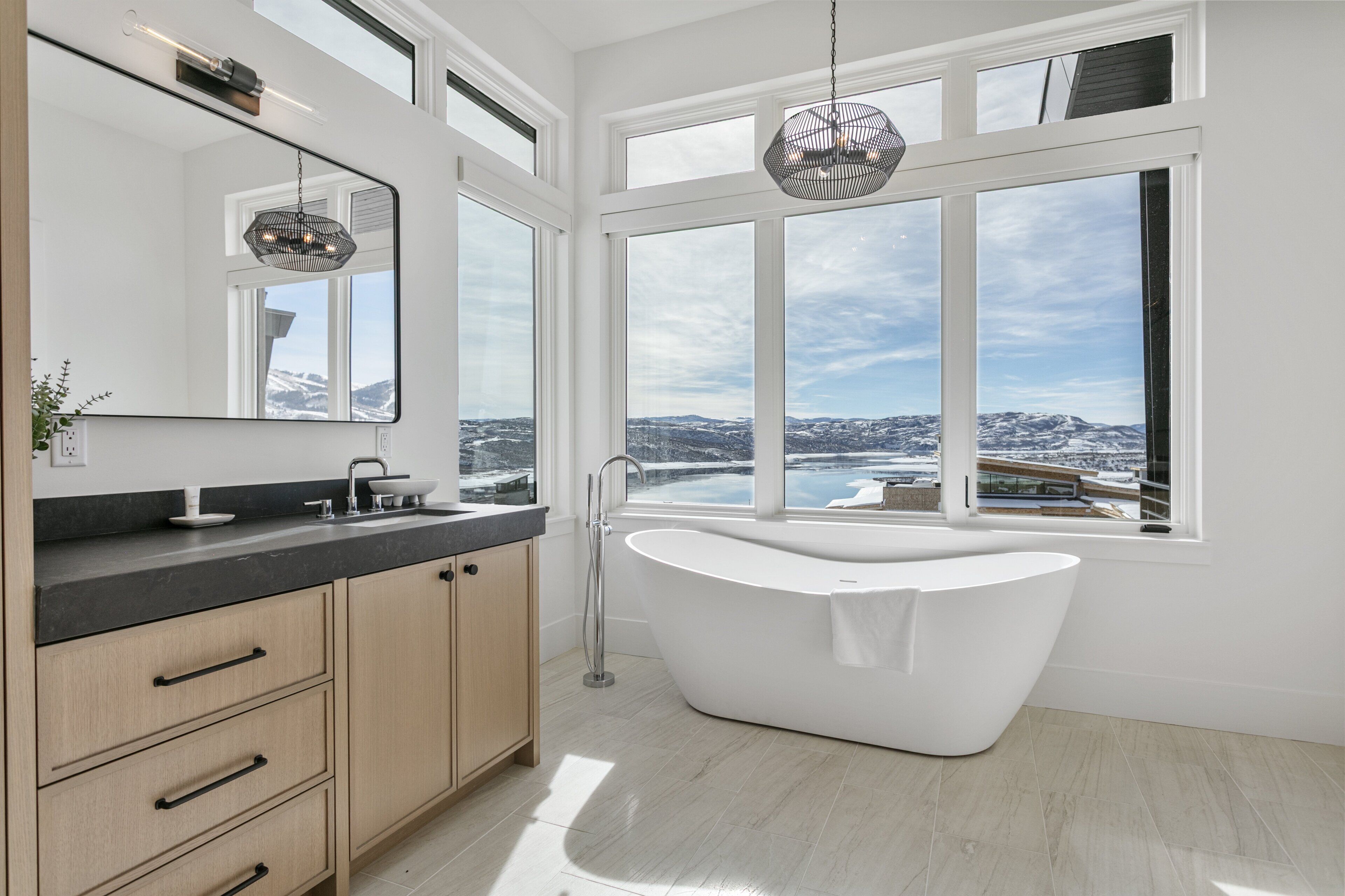 Un baño moderno con una bañera independiente, un espejo grande y vistas a un paisaje nevado a través de amplios ventanales.