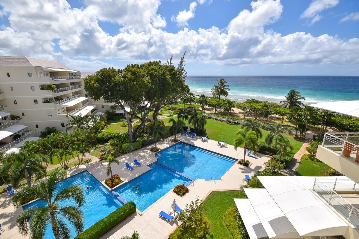 A hotel with a swimming pool, palm trees, and a view of the ocean.
