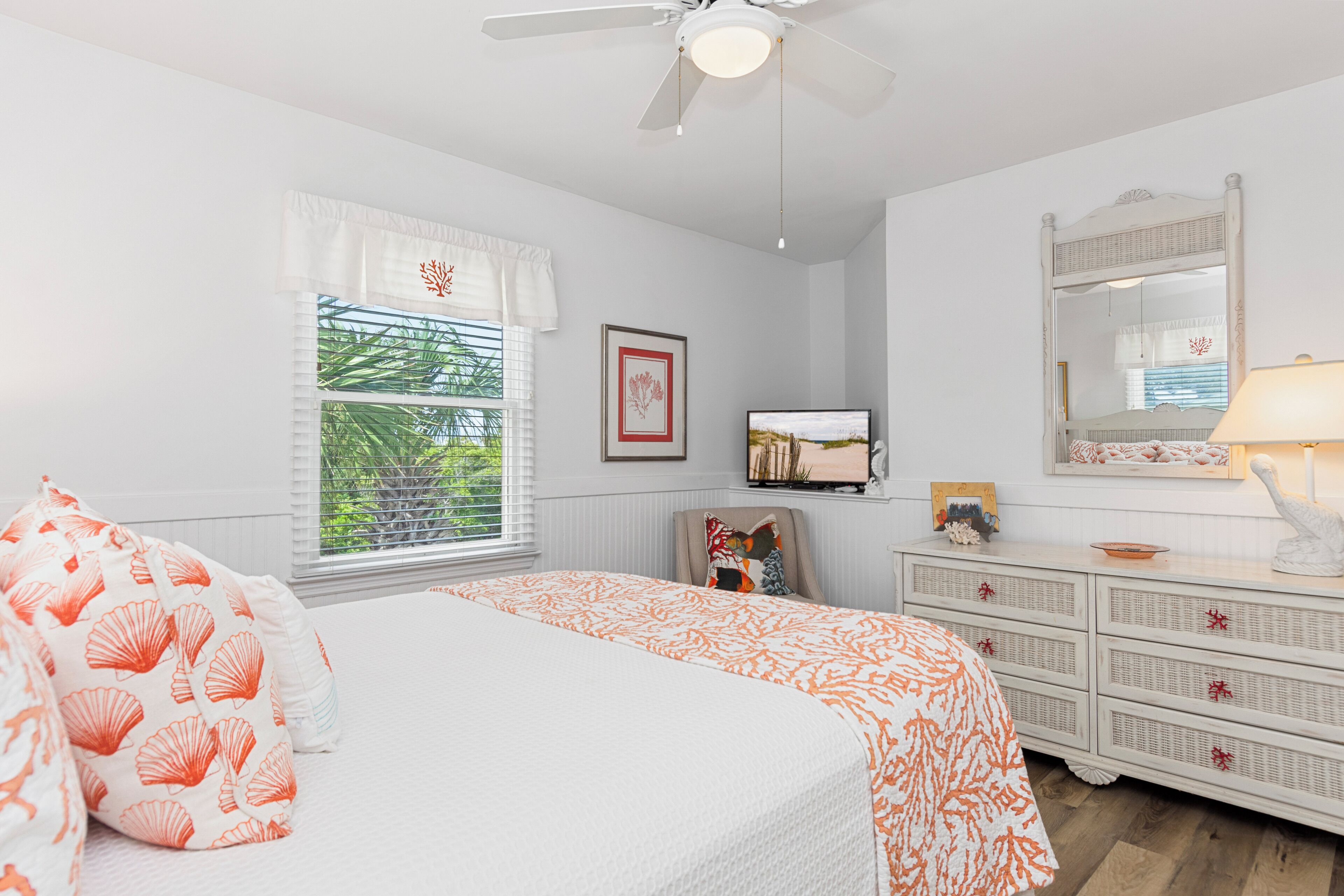 A bedroom with a bed, a dresser, a mirror, a television, and a window with blinds.