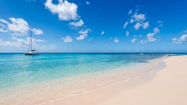 Une plage avec une eau turquoise et limpide et un voilier.