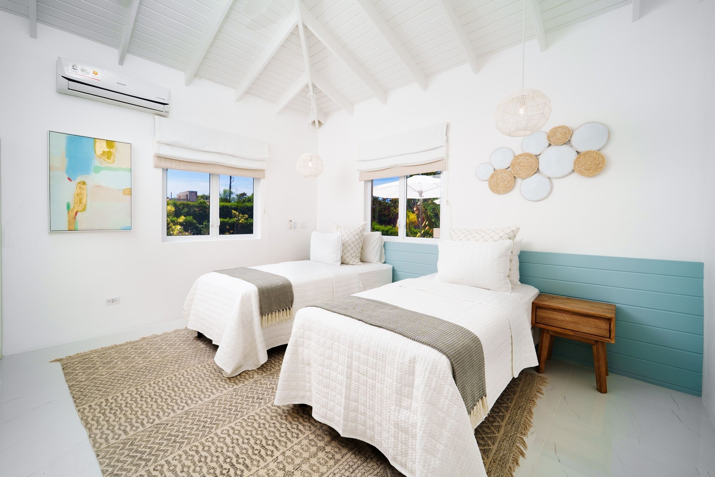 A bedroom with two beds, a wooden nightstand, a wall-mounted air conditioner, and a large window with a view.