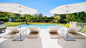 Un espace aménagé au bord de la piscine, avec des chaises longues et des parasols, offrant une vue dégagée sur la piscine et un jardin bien entretenu.