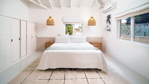 Une chambre à coucher avec un lit, deux tables de chevet, une fenêtre et une vue sur la verdure.
