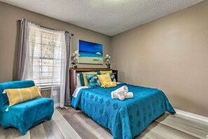Ein Schlafzimmer mit Bett, einem Sessel, einem Gemälde und einem Fenster mit Vorhängen.