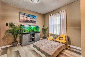 Ein Wohnzimmer mit einem großen Flachbildfernseher, einer Couch, zwei Blumentöpfen und einem Bild an der Wand.