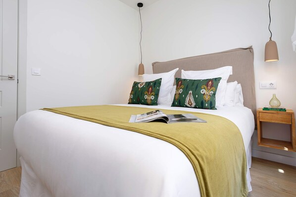 A neatly made bed with a white and green patterned pillow, a magazine on the bed, and a bedside table with a book and a lamp. - Exclusive Duplex With Private Terrace Pool in Seville Feria 21 (Seville)