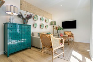 A living room with a teal chest of drawers, a rattan chair, a sofa, a flat-screen TV, and decorative plates on the wall. - Exclusive Duplex With Private Terrace Pool in Seville Feria 21 (Seville)