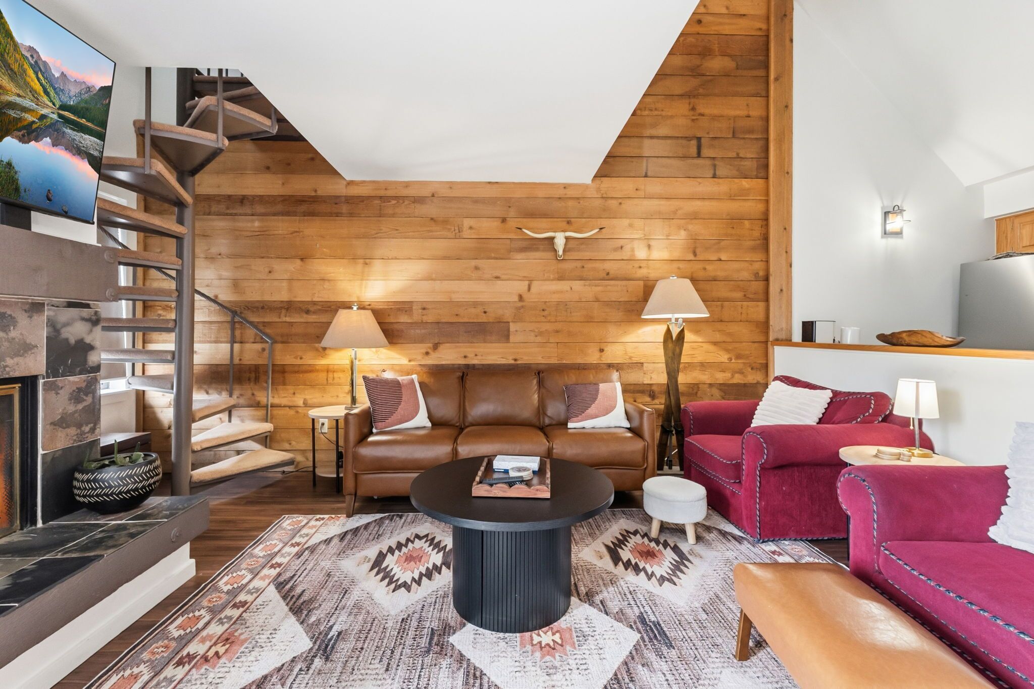 Un salon moderne avec un mur en bois, un canapé, un fauteuil rouge, une table basse et un téléviseur.