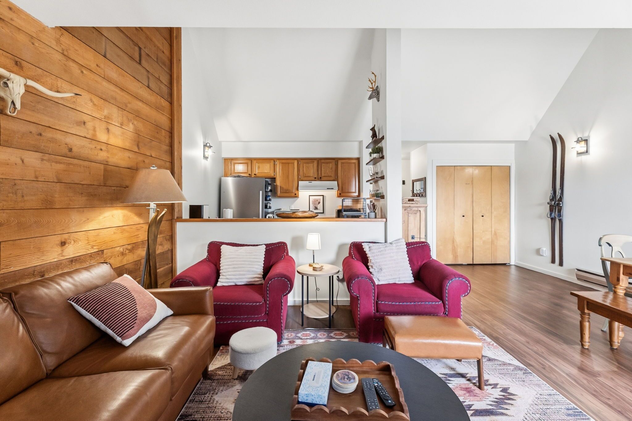 A modern living room with a brown leather sofa, two red armchairs, a coffee table, and a kitchen in the background.