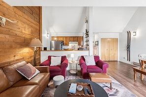 A modern living room with a brown leather sofa, two red armchairs, a coffee table, and a kitchen in the background. - Keystone Lakeside Condo | Outdoor Pool, Shuttle, and Mountain Access (Keystone)