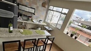 A modern kitchen with a dining area, large windows, and a view of buildings. - Studio apartment in Prainha de Muquiçaba, 5 minutes from Praia do Morro, excellent for couples. (Guarapari)