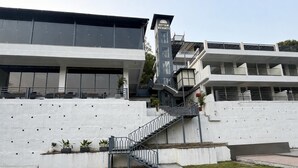 Ein modernes Gebäude mit einer Treppe, die zu einem Balkon führt, einem Schild für Divyam Resorts und einer weißen Wand mit kleinen Löchern.