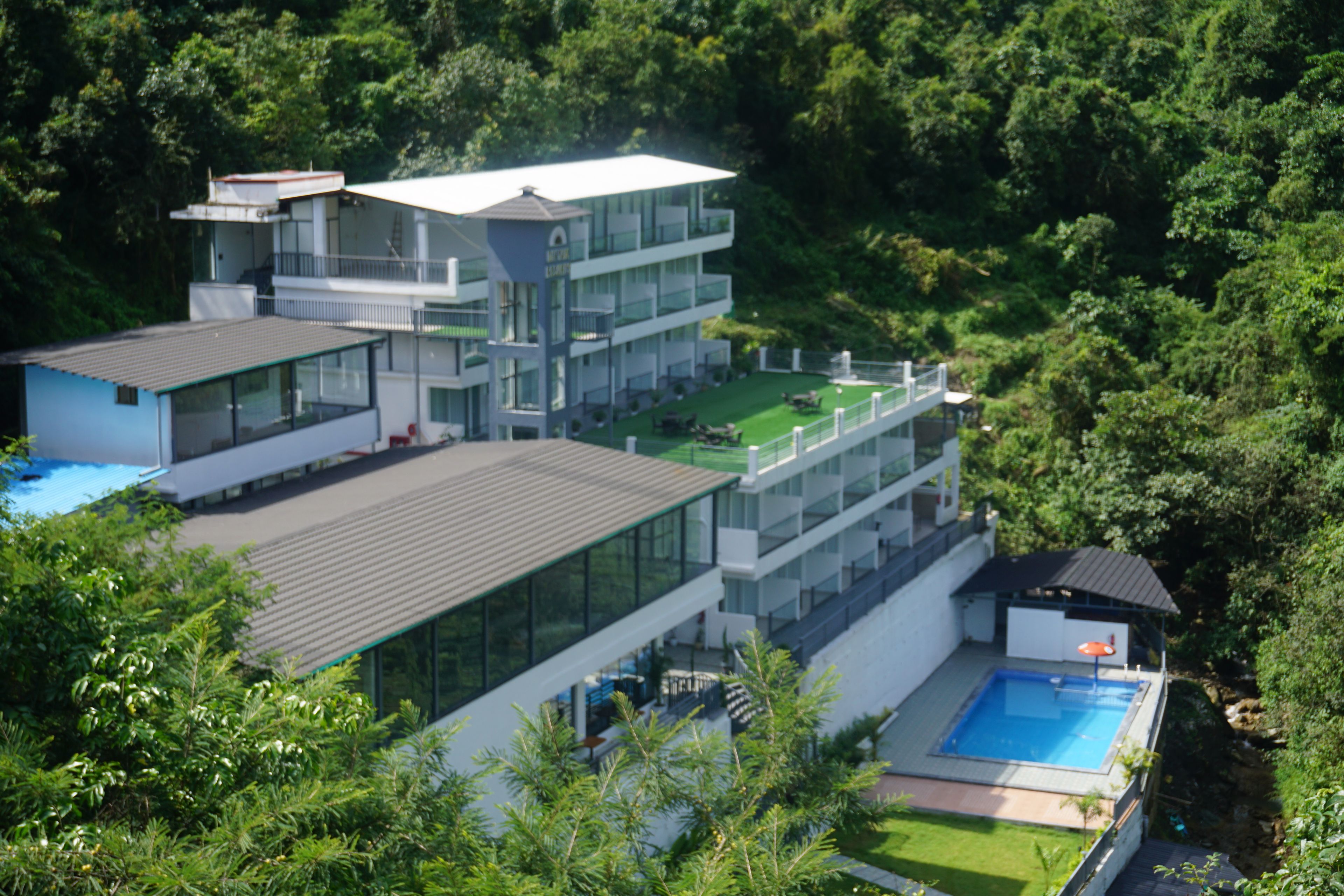 A modern multi-story building with a rooftop pool and a tennis court.