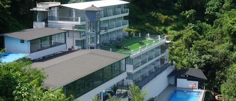 A modern multi-story building with a rooftop pool and a tennis court.