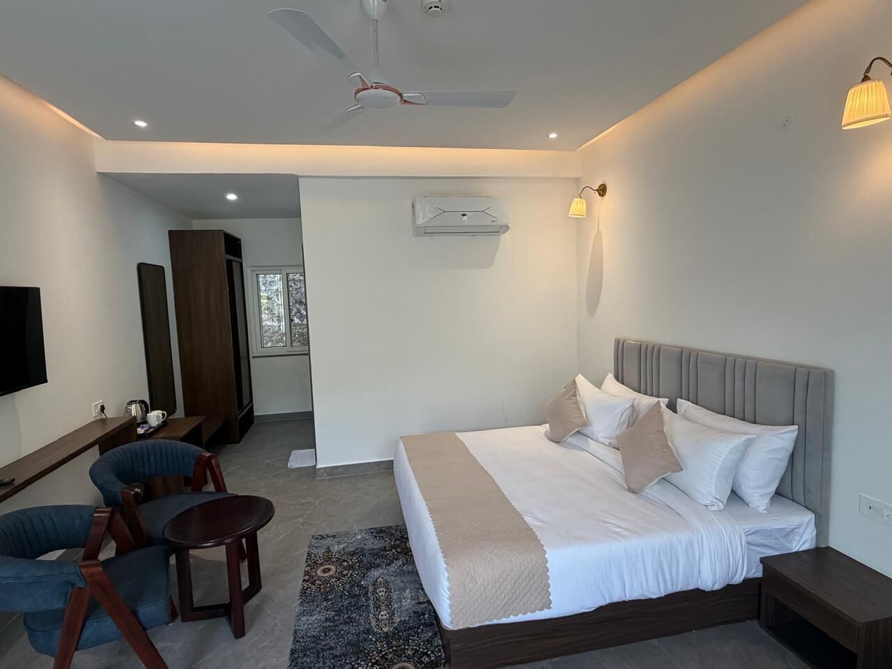 Una habitación de hotel moderna con una cama grande, un escritorio, una silla y un ventilador de techo.