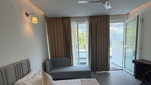 Ein Hotelzimmer mit Bett, Sofa, Schreibtisch und einem Balkon mit Vorhängen.