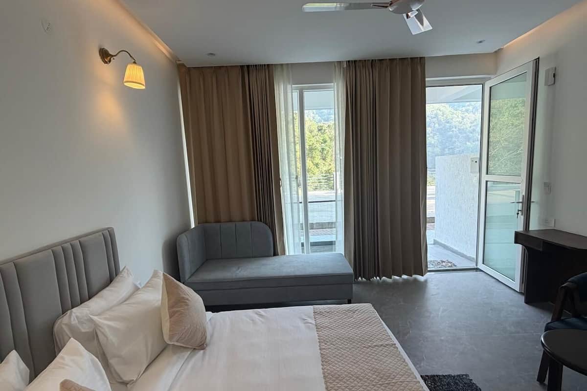 Une chambre d’hôtel avec un lit, un canapé, un bureau et un balcon avec des rideaux.
