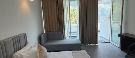 A hotel room with a bed, a sofa, a desk, and a balcony with curtains.