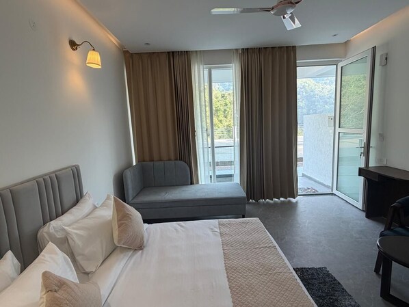 Habitación de hotel con cama, sofá, escritorio y balcón con cortinas.