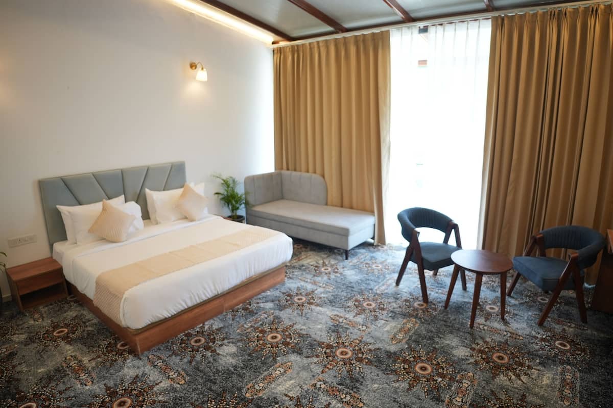 Une chambre d’hôtel comprenant un lit, un canapé, deux fauteuils, une petite table et une moquette à motifs.