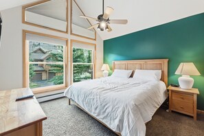 A bedroom with a bed, nightstands, a ceiling fan, and a view of a house through large windows. - Keystone Mtn Retreat w/ Hot Tub and Views! (Keystone)