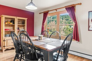 A dining area with a wooden table, black chairs, a wooden cabinet with dishes, and a window with curtains. - Keystone Mtn Retreat w/ Hot Tub and Views! (Keystone)