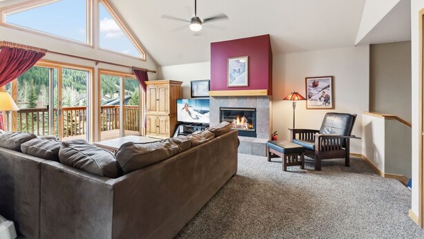 Una sala de estar con chimenea, un sofá, un televisor y vistas al exterior.