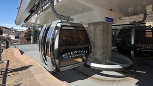 Une station de téléphérique avec une enseigne indiquant « Riverfront Village », une zone d’attente couverte et un ciel dégagé.