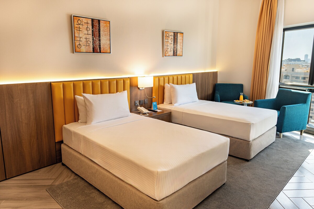 A hotel room with two beds, a nightstand, a chair, and artwork on the walls.