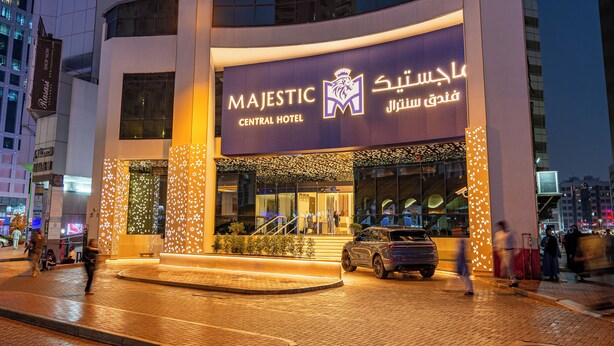 The exterior of the Majestic Central Hotel with a prominent entrance, a car parked in front, and a cityscape in the background.