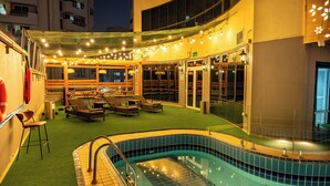 A rooftop pool area with a swimming pool, lounge chairs, and a covered seating area.