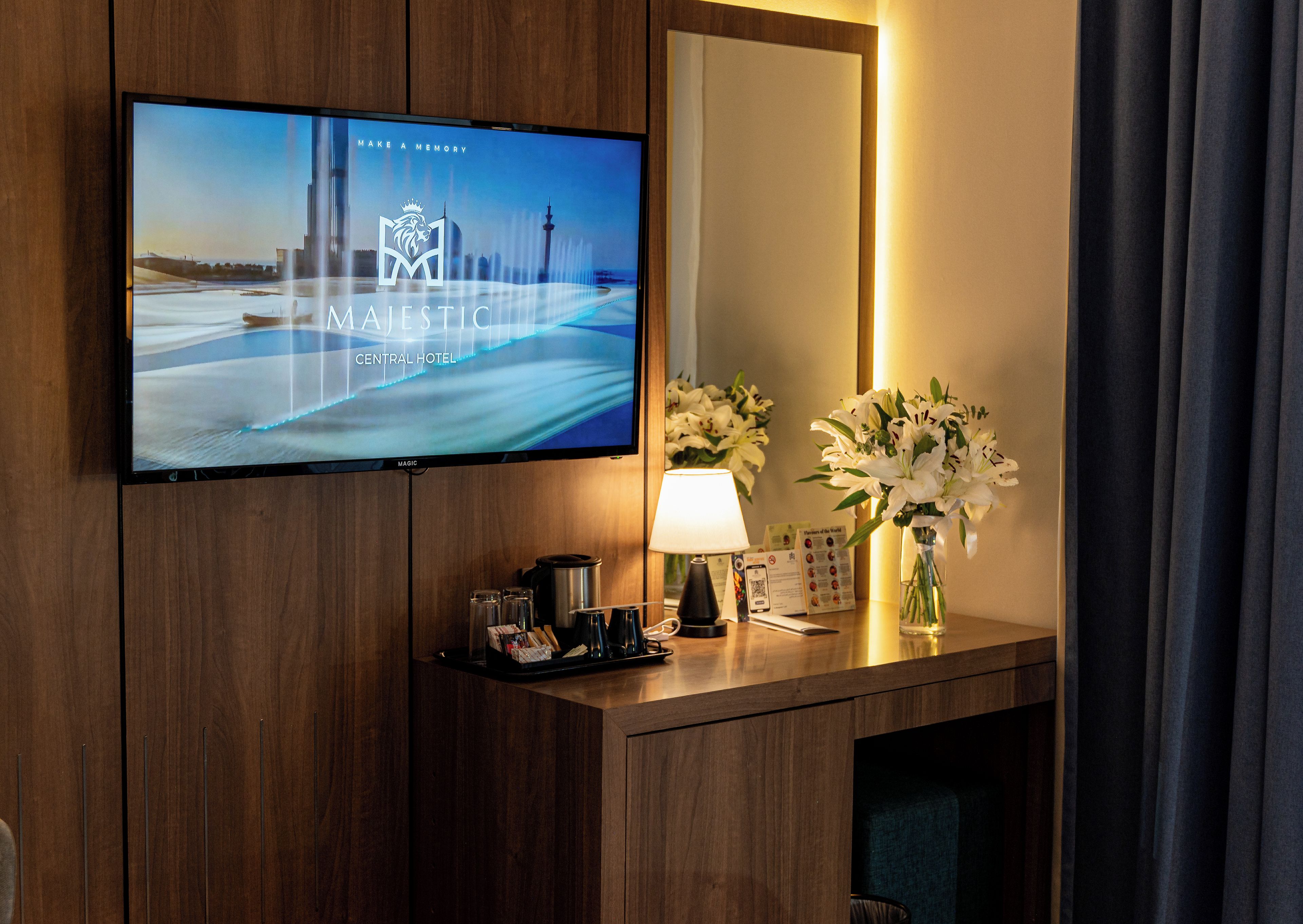 Une chambre d’hôtel dotée d’un téléviseur à écran plat fixé à un mur en bois, d’une table de chevet avec une lampe et un vase de fleurs, et d’un miroir qui reflète la pièce.