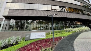 A modern building with a curved facade, a sign reading "LIBERTY," and a landscaped area with plants and a paved walkway. - LK Santo Agostinho 4 (Belo Horizonte)