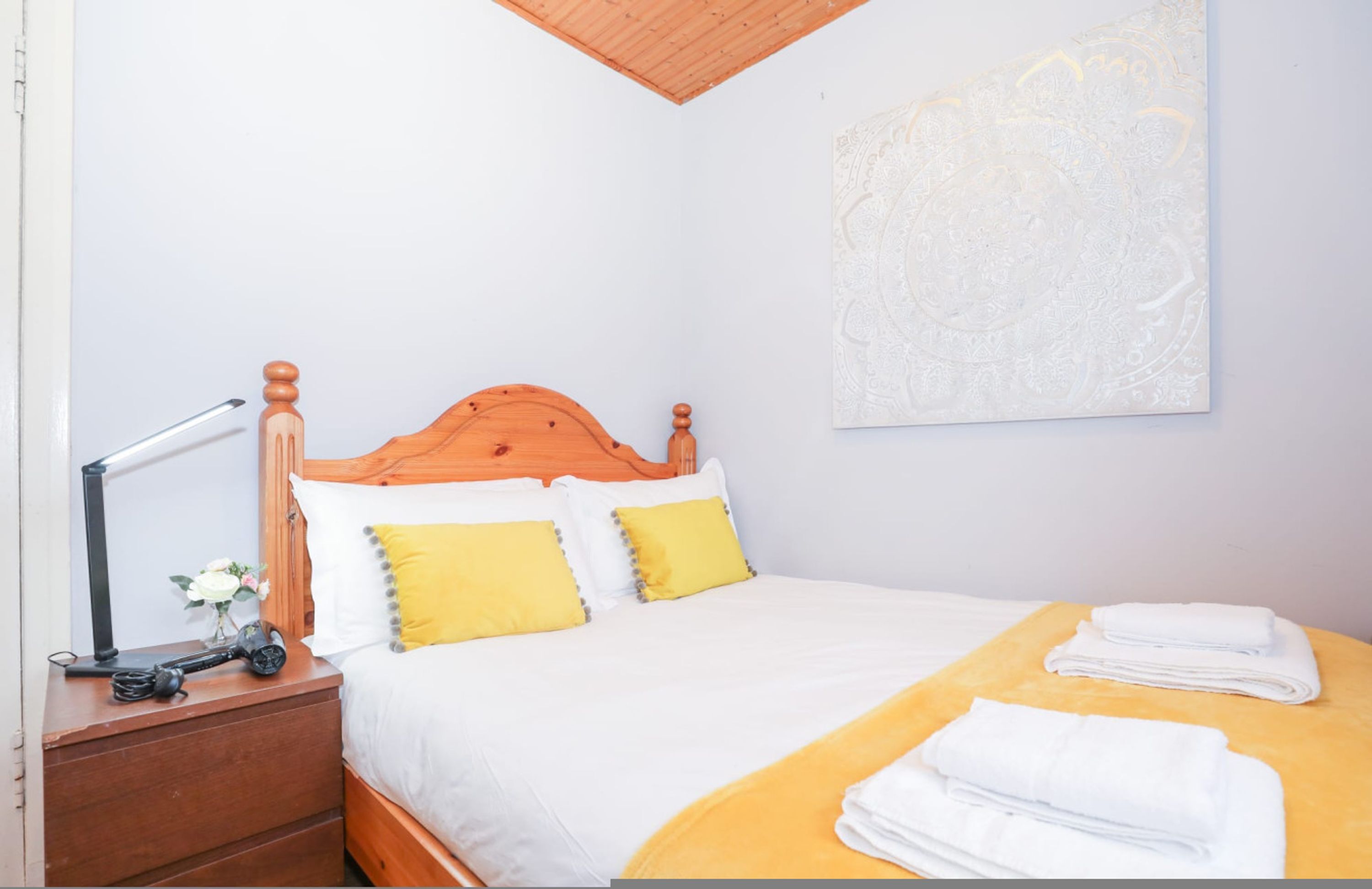 A bedroom with a wooden bed, white bedding, a yellow throw blanket, and a wall-mounted artwork.