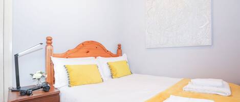A bedroom with a wooden bed, white bedding, a yellow throw blanket, and a wall-mounted artwork.