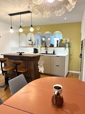 Une cuisine moderne dotée d’un îlot central, de luminaires suspendus et d’un coin repas avec une table et des chaises.