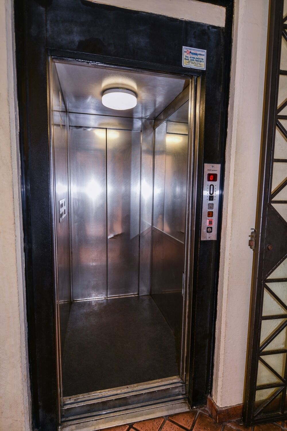 Un ascensor con panel de control, interior metálico y puerta con panel de vidrio.